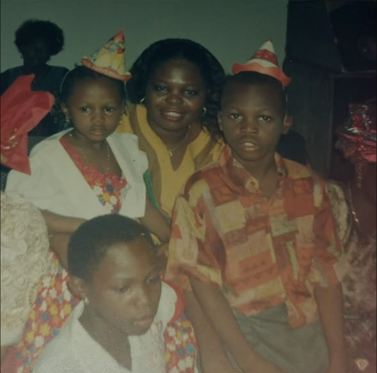 An older celebration photograph of a smiling woman surrounded by children, two wearing party hats.
